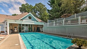 A swimming pool with clear blue water, a covered patio area, and a fenced deck with outdoor seating.