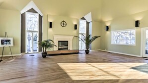 A spacious room with high ceilings, large windows, a fireplace, and potted plants.