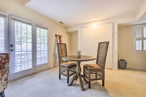 A room with a round table and two wicker chairs, a door with blinds, and a carpeted floor. - Lovely Norwich Villa, On Golf Course w/ Amenities! (Norwich)