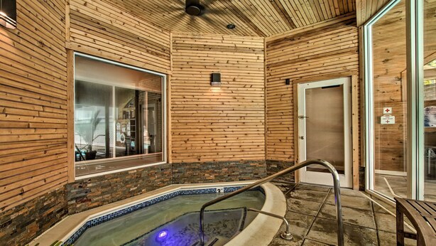 A wooden interior with a hot tub, a glass door, and a metal railing.