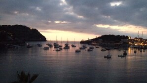A coastal marina at dusk with boats anchored in calm waters, a hilly landscape in the background, and a small settlement with lights on the right. - Spacious apartment with large terrace and summer kitchen (Port de Sóller)