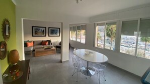 A spacious living area with a dining table and chairs, a sofa, and a large window offering a view of a parking lot. - Spacious apartment with large terrace and summer kitchen (Port de Sóller)