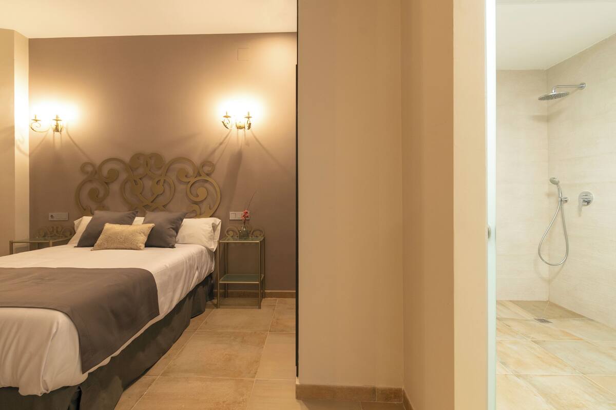 Una habitación de hotel con cama, mesitas de noche y un espacio para la ducha.