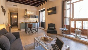 A modern living room with a sofa, a coffee table, a laptop, and a dining area with chairs and a kitchen in the background. - Palacete 1620, Apartamentos Premium-Only adults (Granada)