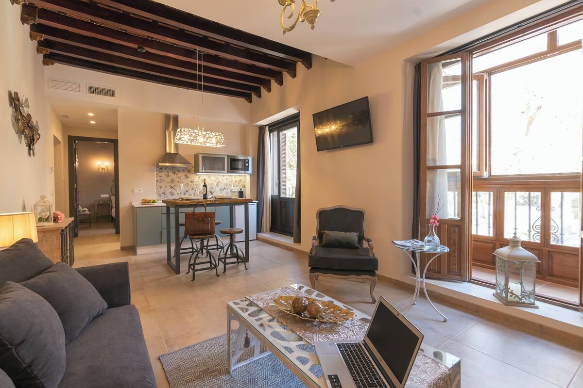 Una sala moderna con sofá, mesa de centro, una computadora portátil y un comedor con sillas, con una cocina al fondo.