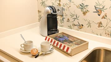 Une machine à café, deux tasses, une cuillère et une boîte de sachets de thé Nespresso sont posés sur un comptoir.