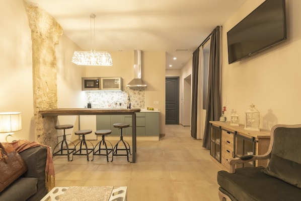 A modern kitchen with a central island, bar stools, a microwave, and a hanging light fixture. - Palacete 1620, Apartamentos Premium-Only adults (Granada)