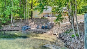 A clear stream with a wooden deck and chairs, surrounded by trees and a building in the background. - 4 Bedrooms, 1 Flex Room, 4 Bathrooms!  Beautiful Home with SANDY BEACH!  Occupancy 8! HOT TUB! (Huddleston)