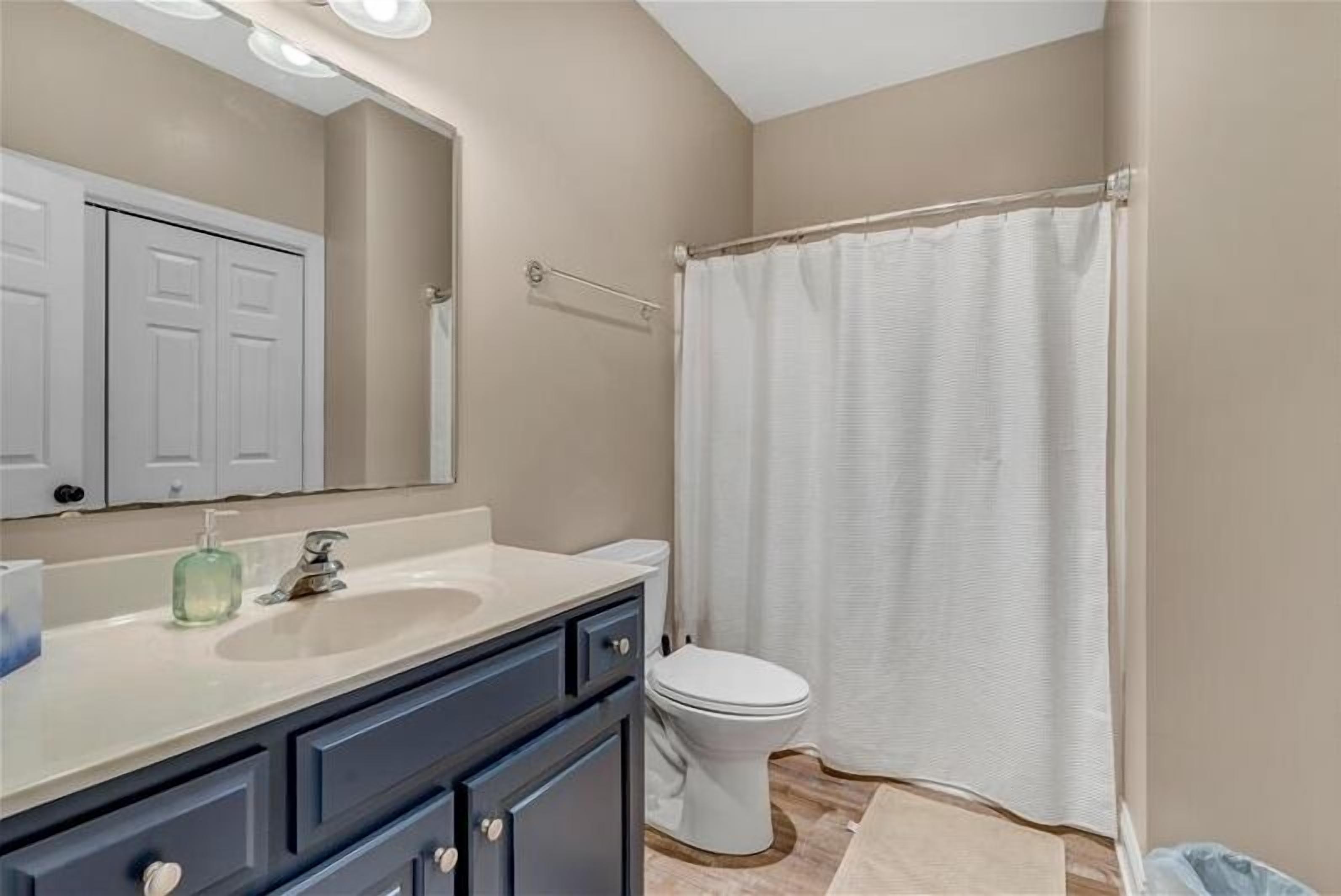 A bathroom with a white toilet, a sink with a mirror above it, and a shower curtain.