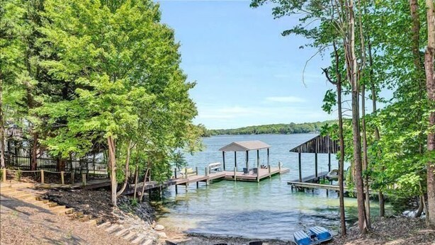 A lakeside property with a dock, outdoor seating, and a covered area. - 4 Bedrooms, 1 Flex Room, 4 Bathrooms!  Beautiful Home with SANDY BEACH!  Occupancy 8! HOT TUB! (Huddleston)