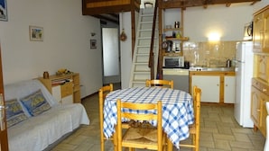 A cozy room with a dining table, chairs, a sofa, a kitchen area, and a staircase. - Semi-detached duplex house of 50m² for 5 people (BISCARROSSE)