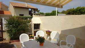 An outdoor patio with a table and white plastic chairs, a potted plant, and a barbecue grill. - Semi-detached duplex house of 50m² for 5 people (BISCARROSSE)