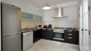 A compact kitchen with a stainless steel refrigerator, a dishwasher, a microwave, a toaster, a coffee maker, and a stove.