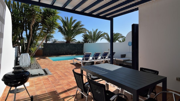 An outdoor patio with a pool, lounge chairs, and a barbecue grill.
