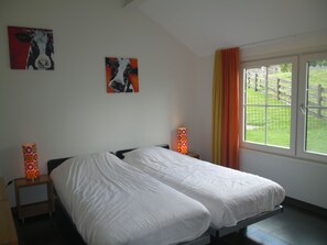 A bedroom with a double bed, two wall-mounted lamps, and two paintings.