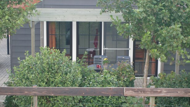 Une maison dotée d’un patio couvert, d’une clôture en bois et d’une fenêtre donnant sur un jardin.