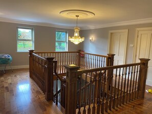 A spacious room with a wooden staircase, large windows, and a chandelier.