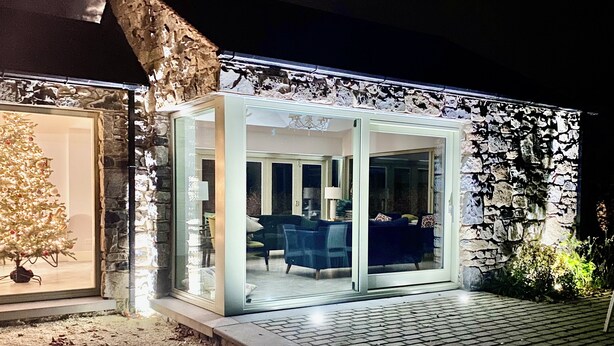 A glass-enclosed patio with a stone wall, a Christmas tree, and a seating area with chairs and a table. - Beautiful 5 bedroom home in Mid Ulster- Magherafelt  (County Derry)