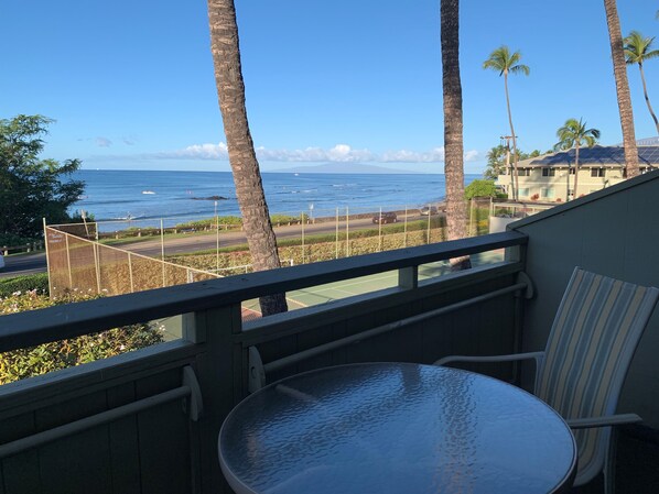 A balcony with a view of the ocean, palm trees, and a tennis court.