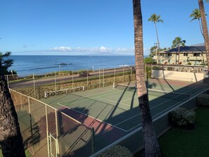 A tennis court with a view of the ocean and a building with a sloped roof.