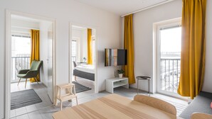 A modern hotel room with a bed, a TV, a desk, a chair, and a balcony with yellow curtains. - Hiisi Homes Turku Elin Sagerin kuja (Turku)