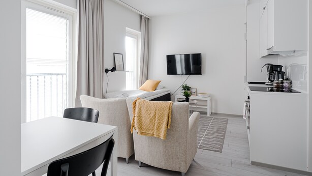 A modern, well-lit room with a dining area, a sofa, a TV, and a kitchenette. - Hiisi Homes Turku Elin Sagerin kuja (Turku)