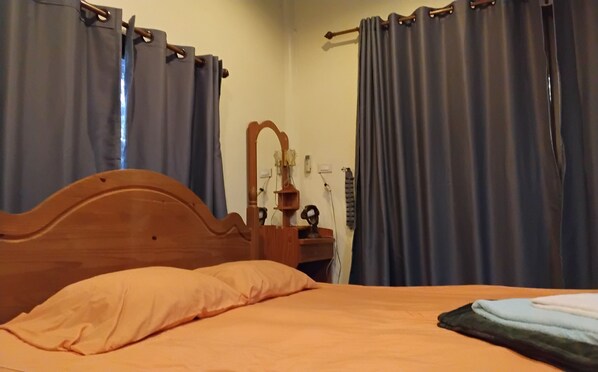 A bedroom with a wooden headboard, a bed with an orange bedspread, and a nightstand with a mirror and a lamp.