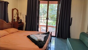 A bedroom with a bed, a nightstand, a mirror, a window with curtains, and a view of the outdoors. - Garden Lodge Bungalow (Klong Son)