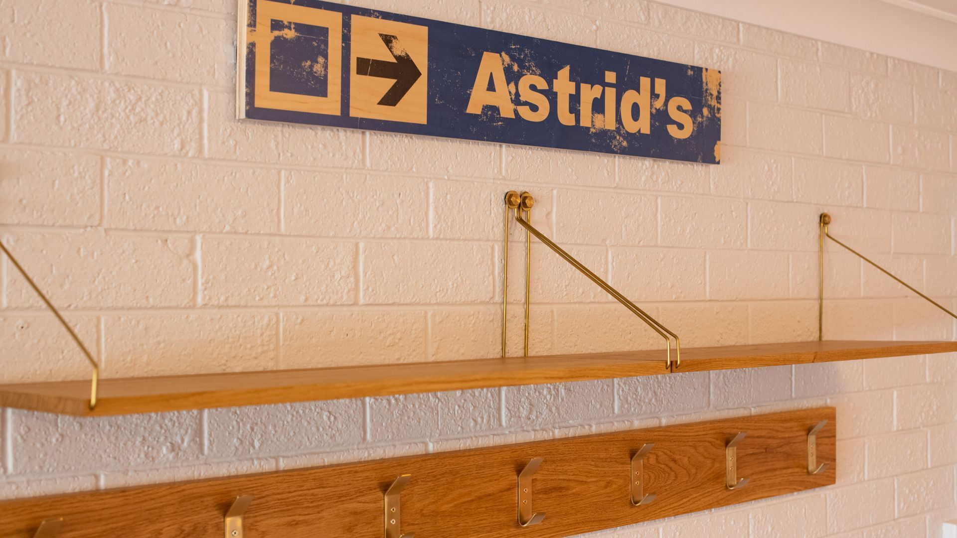Un letrero en la pared con la palabra 'Astrid's' y flechas direccionales. Abajo, una estantería de madera con ganchos metálicos.