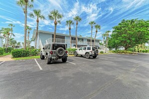 Um estacionamento com dois SUVs, palmeiras e um edifício com varanda.