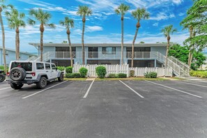 A two-story building with a parking lot, a white fence, and palm trees. - West Bay Cove 226 · Kayak Launch · For Sale (Holmes Beach)