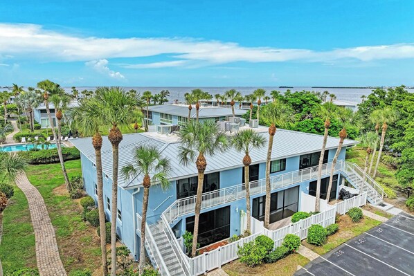 A multi-story building with a pool, surrounded by palm trees, overlooking a body of water.