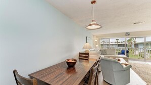 Ein Essbereich mit Holztisch und -stühlen, einer hängenden Leuchte und Blick auf ein Gebäude durch große Fenster.