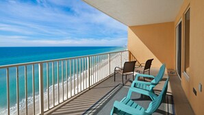 A balcony with a view of the ocean, two chairs, and a table.