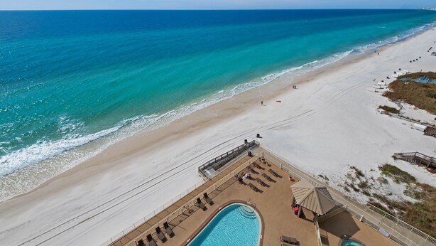A beach resort with a swimming pool, sun loungers, and a view of the ocean.