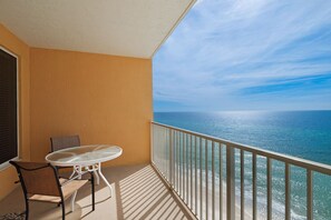 Un balcón con mesa y sillas, con vista a un mar azul y despejado.