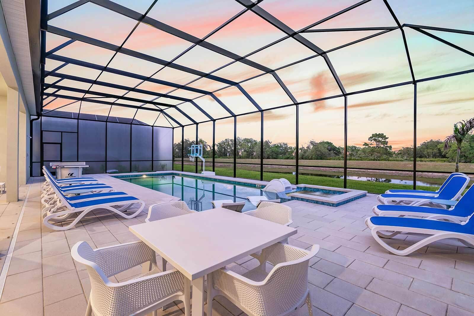 An outdoor pool area with lounge chairs and a table, surrounded by a glass enclosure.