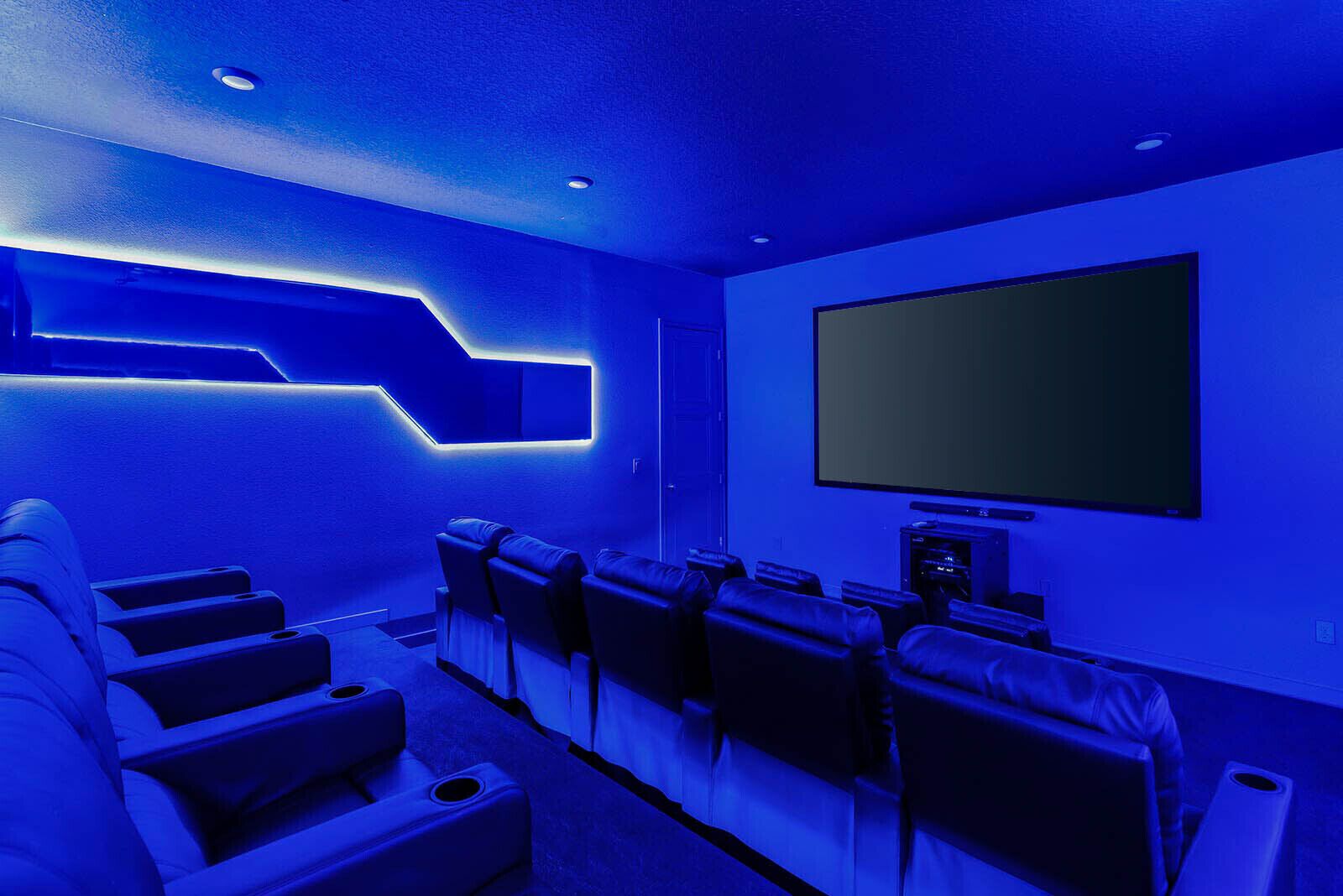 Sala de cine en casa con una pantalla grande, sillones reclinables y un diseño moderno con iluminación azul.