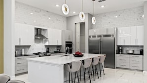 A modern kitchen with white cabinetry, a central island with bar stools, stainless steel appliances, and pendant lighting. - Homes by Villatel | Trampoline RM, Bowling, Ocean Theme BR, Theater, Near Parks (Davenport)