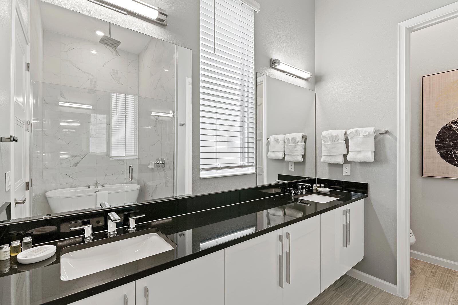 A modern bathroom with a black countertop, white cabinets, a large mirror, and a glass-enclosed shower.