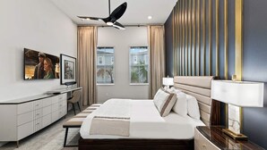 A modern bedroom with a large bed, a desk, a television, and a ceiling fan. - Homes by Villatel | Trampoline RM, Bowling, Ocean Theme BR, Theater, Near Parks (Davenport)