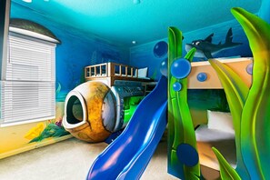 A room with a bunk bed, a slide, and a window with blinds. - Homes by Villatel | Trampoline RM, Bowling, Ocean Theme BR, Theater, Near Parks (Davenport)