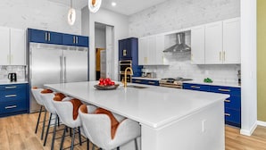 Une cuisine moderne dotée d’un grand îlot central, d’appareils électroménagers en acier inoxydable et de meubles de rangement bleus.