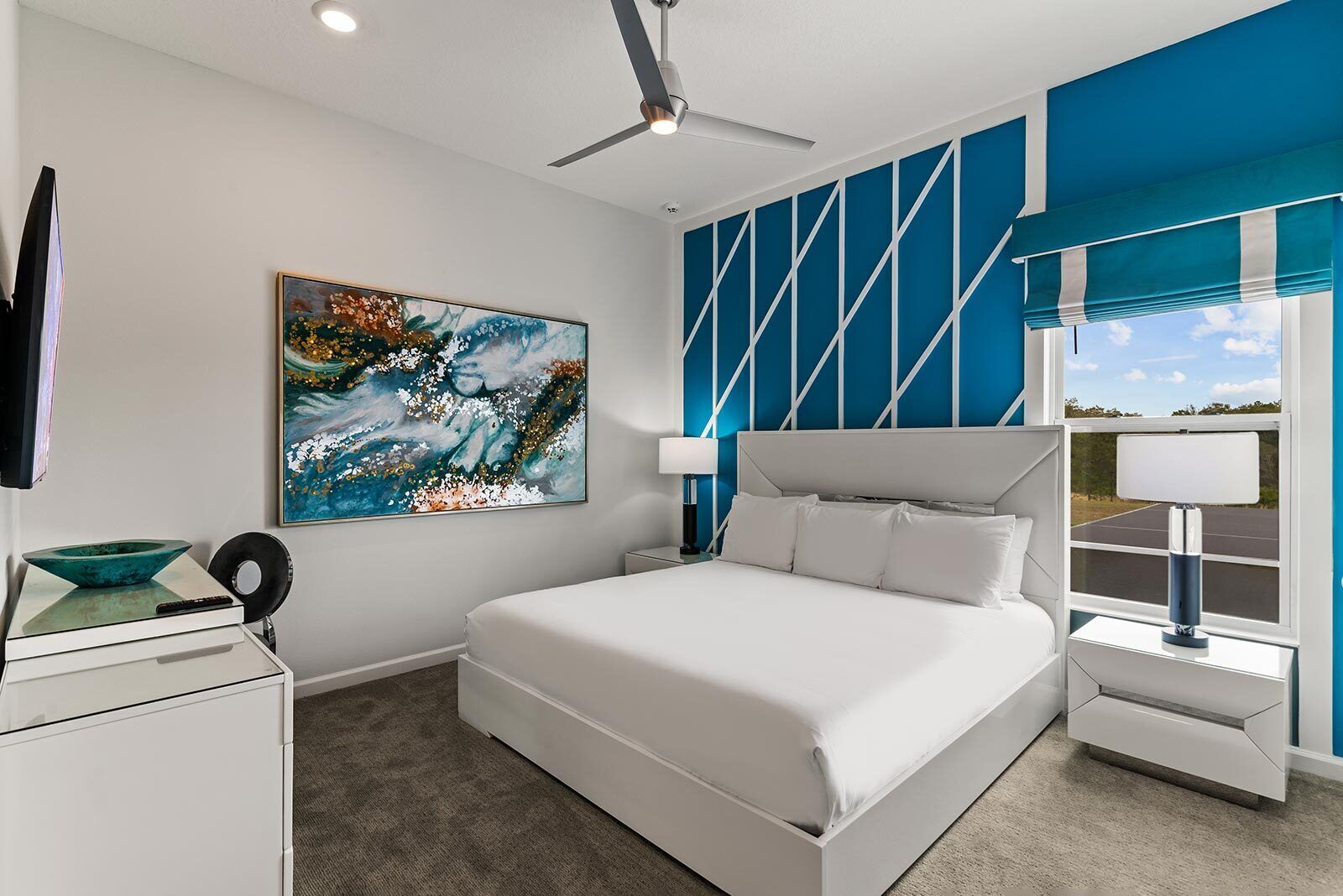 Une chambre d’hôtel moderne avec un grand lit, un ventilateur de plafond, un tableau et une vue sur l’extérieur.