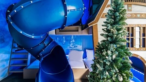 Ein Zimmer mit einer blauen Spirale, einem Weihnachtsbaum und einem Bett an einer blauen Wand, mit einem Gemälde einer verschneiten Landschaft.