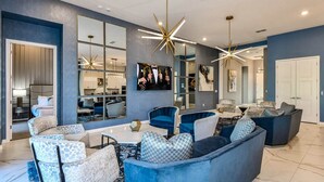 A modern living room with blue sofas, a coffee table, and a TV mounted on the wall. - Feature-Rich Home w Superhero Theme BR, Huge Arcade & Theater - Near Disney (Davenport)