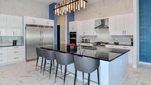 A modern kitchen with a central island, stainless steel appliances, and a unique pendant light. - Feature-Rich Home w Superhero Theme BR, Huge Arcade & Theater - Near Disney (Davenport)