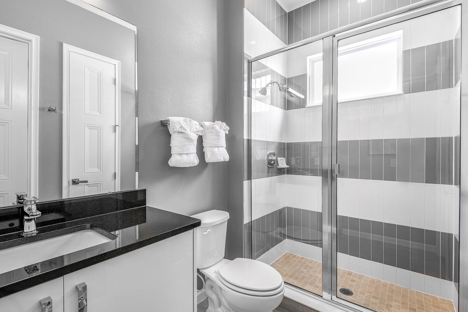 A modern bathroom with a glass-enclosed shower, a toilet, and a sink with a black countertop.