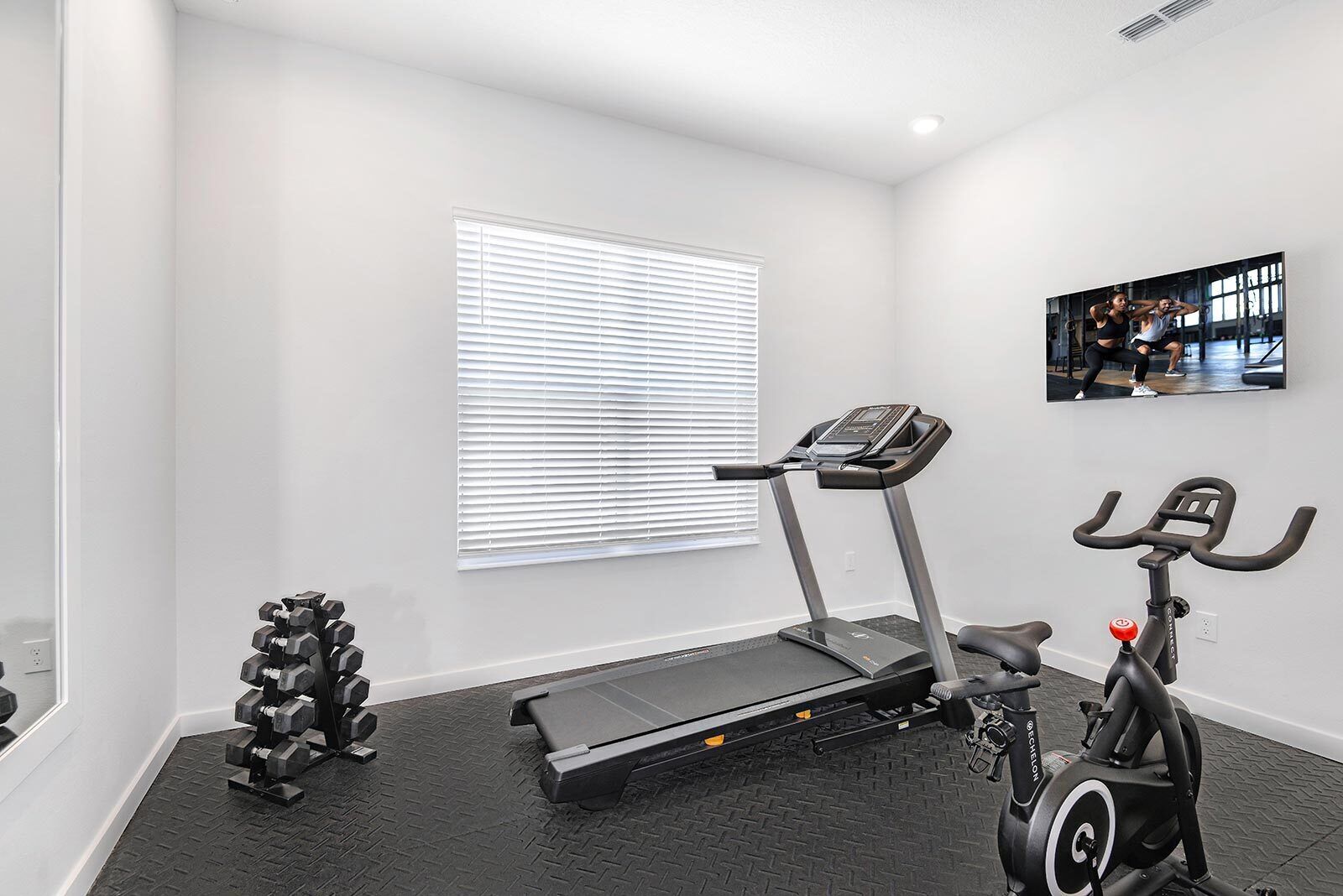 Une salle de sport à domicile équipée d’un tapis de course, d’un vélo d’appartement et d’haltères.