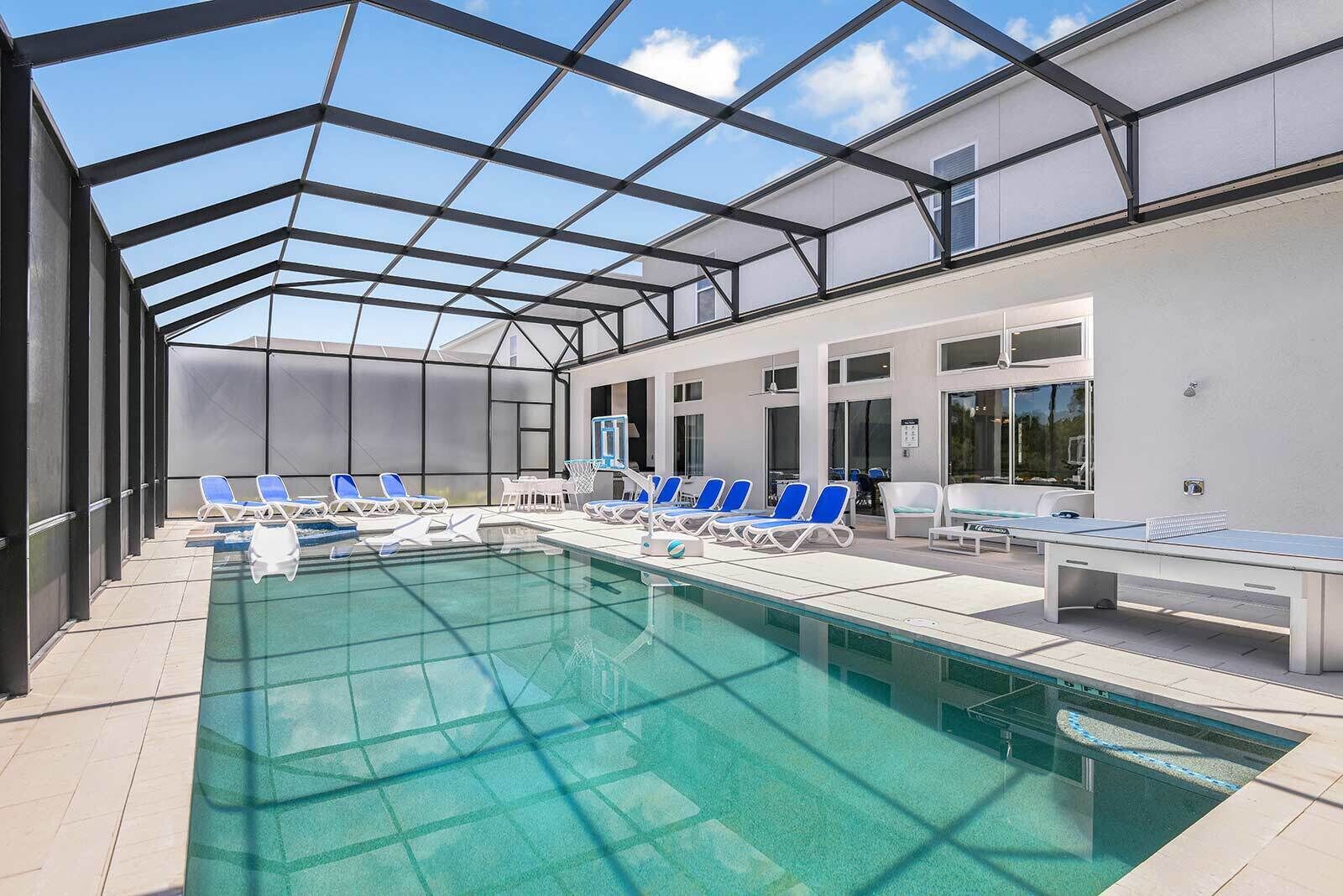 Une piscine avec des chaises longues bleues et un panier de basketball.